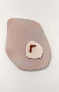 Pieza de cerámica plana ovalada, compuesta por tres elementos. Uno grande de color rosacéo sobre el que están uno más pequeño blanco, plano, y una pieza pequeña rojiza en forma de L