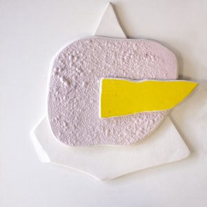 Pieza escultura de cerámica en tres colores para colgar en la pared de 3 colores. 1 blanco en forma de triangulo, sobre este una pieza casi redonda rosa y sobre este, otra pieza más pequeña amarilla.